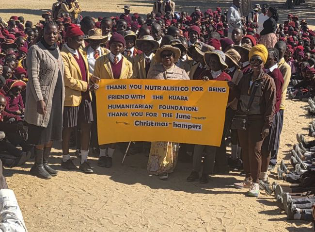Children at a KHF-supported school holding the yellow Naturalistico thank-you banner during a Christmas hamper distribution